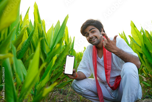 Indian farmer showing smart phone screen at green turmeric agriculture field.