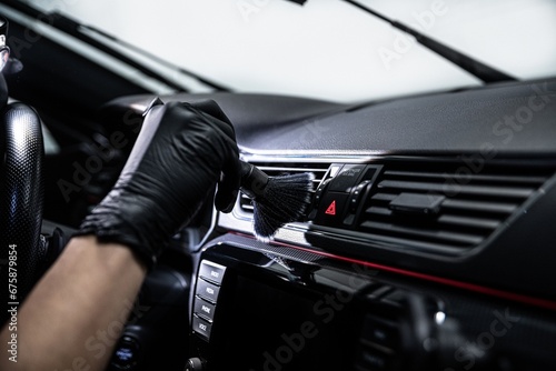 Car wash employee or a car detailing studio worker carefully cleans the air vents inside a car with a brush photo