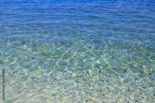 Sunny water waves with stones on a bottom. Summer vacation. Abstract water surface. Water waves background. Water waves with shining pattern texture background. Sea