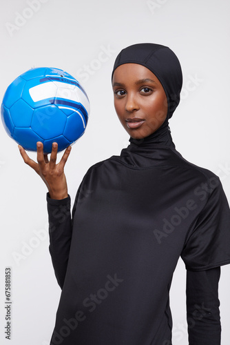 Studio portrait of young woman in hijab holding soccer ball