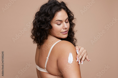 Studio shot of young woman applying moisturizer on arm