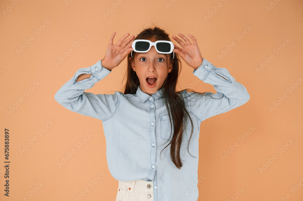In sunglasses, surprised. Cute young girl is in the studio against background In sunglasses, surprised. Cute young girl is in the studio against background