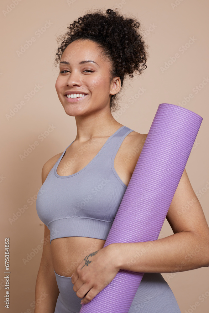 Studio portrait of smiling athletic woman with yoga mat