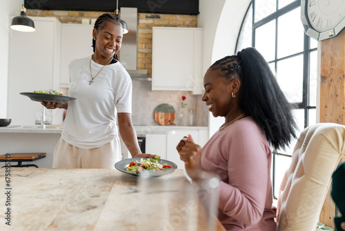 Smiling woman serving dinner for girlfriend at home