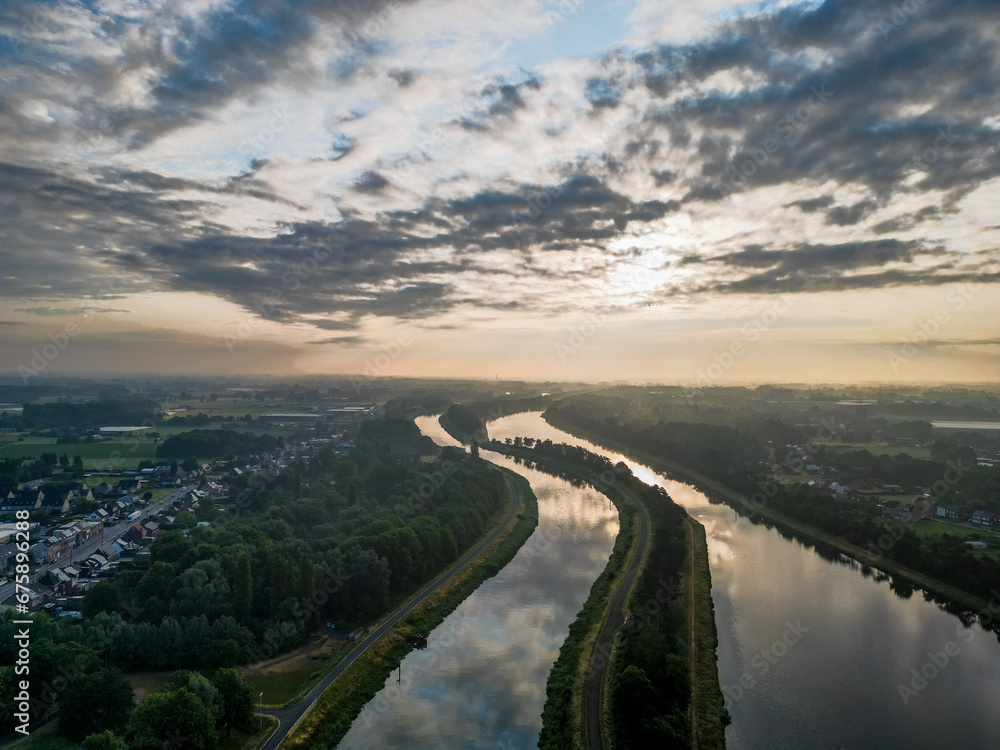 As dawn unfolds, an aerial perspective reveals a breathtaking scene where two waterways, the river and the canal, become mirrors to the heavens. The sunrise spills a spectrum of dramatic colors across