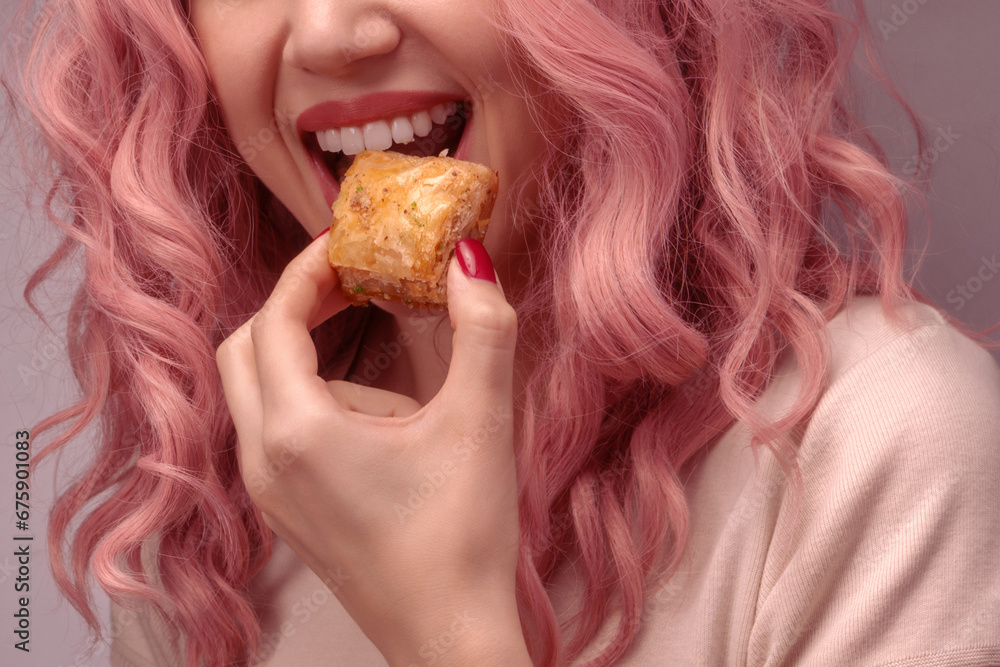 Woman with pink curly hair is eating baklava. Woman with pink curly hair is eating baklava.