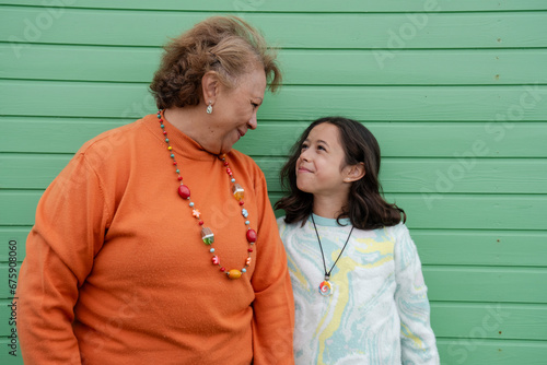 Portrait of grandmother standing with granddaughter against green wall photo