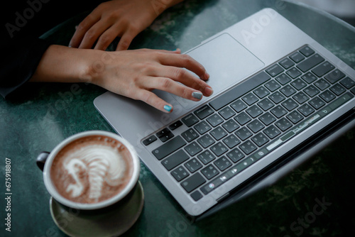 A woman works and types on a laptop keyboard with a coffee cup on the table.