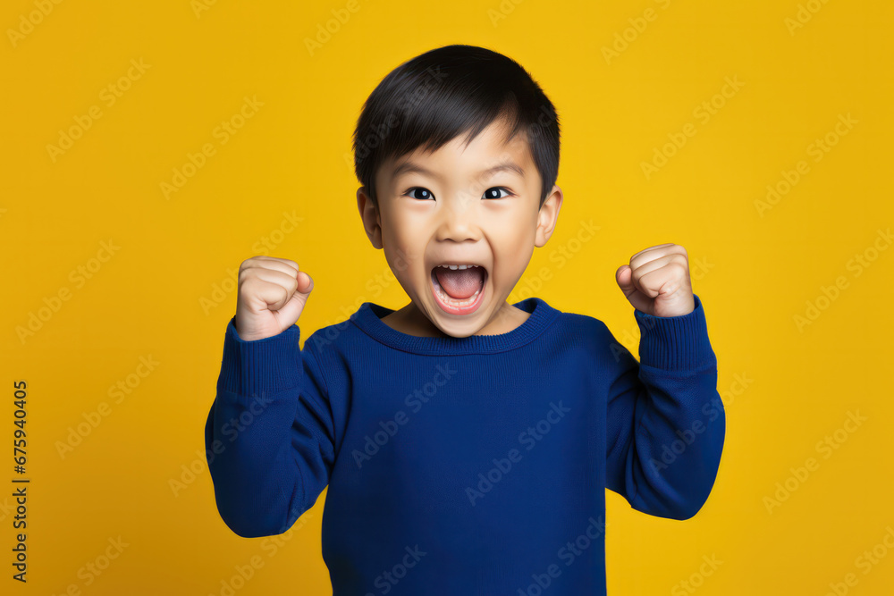 Asian Boy in Blue Sweater Raises Fist on Yellow Background