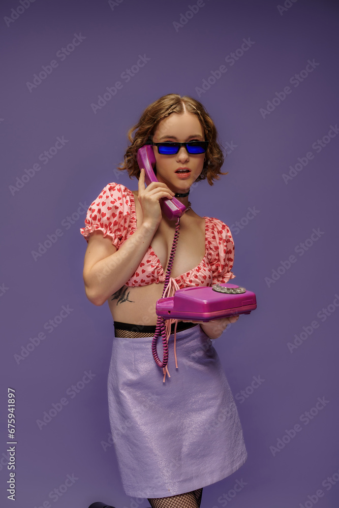 pretty girl in trendy sunglasses and cropped top with hearts talking on retro telephone on purple pretty girl in trendy sunglasses and cropped top with hearts talking on retro telephone on purple