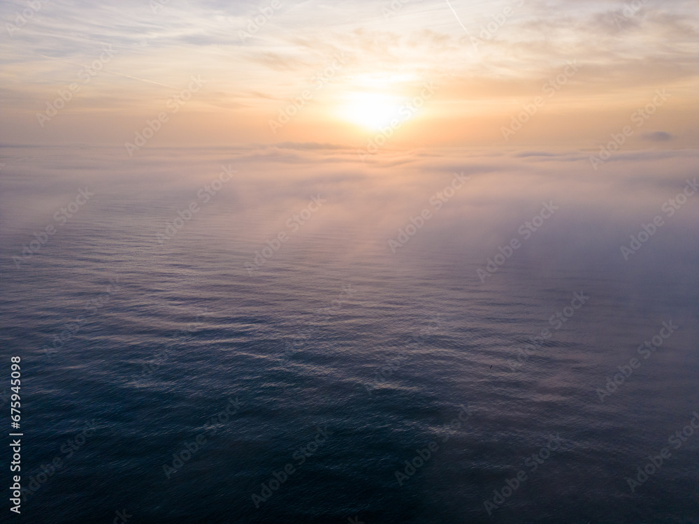 Aerial view of a sunrise sea with a blanket of morning fog and morning sunbeams shining through