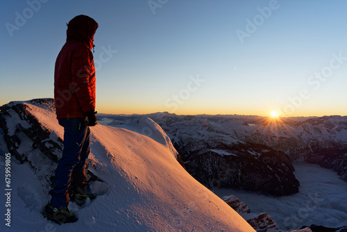 Bergsteiger blickt in Richtung Sonne am Watzmann Hocheck in den Berchtesgadener Alpen zum Sonnenaufgang bei schneebedecktem Panorama im Winter