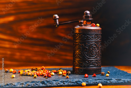 Fototapeta Naklejka Na Ścianę i Meble -  Old metal pepper and spice mill on slate tiles, on a wooden background.
