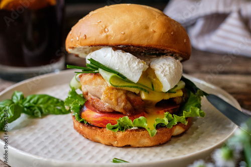 Homemade burger with cheese, lettuce, cucumber, tomato, chicken, poached egg. Wooden background, side view.