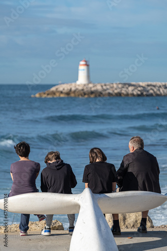Family on whale tail shaped bench by the sea with a lighthouse at the end of a pier