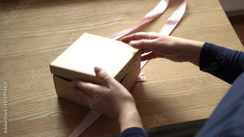 Close-up of woman's hands opening a gift with a pink ribbon. Give gifts. The buyer looks at his order. Purchasing skincare products photo