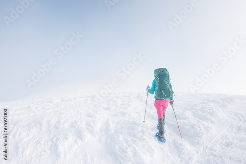 Climber in the mountains. A girl with a backpack and snowshoes walks through the snow.