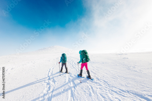 winter activity. Two women walking in snowshoes in the snow, winter hiking, two people in the mountains in winter. © zhukovvvlad