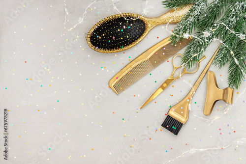 Hairdressing tools in gold on gray concrete background. Hair salon accessories in the corner and copy space. Winter holiday flatlay with fir branches, garland. Idea for congratulations.