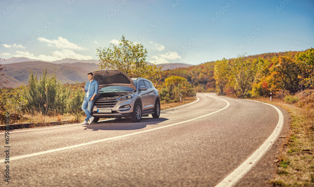 Man standing in front of an open hood of a car on an open road Man standing in front of an open hood of a car on an open road