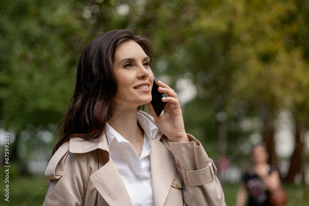 A charming young woman uses a smartphone, with a face, beaming with joy, talks with a friend or colleague and hears happy news. A cute smiling girl is walking in spring park for positive mood. Close A charming young woman uses a smartphone, with a face, beaming with joy, talks with a friend or colleague and hears happy news. A cute smiling girl is walking in spring park for positive mood. Close