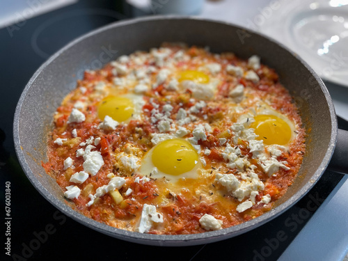 Traditional shakshuku with fried eggs, tomato sauce and sheep's cheese in a pan close up