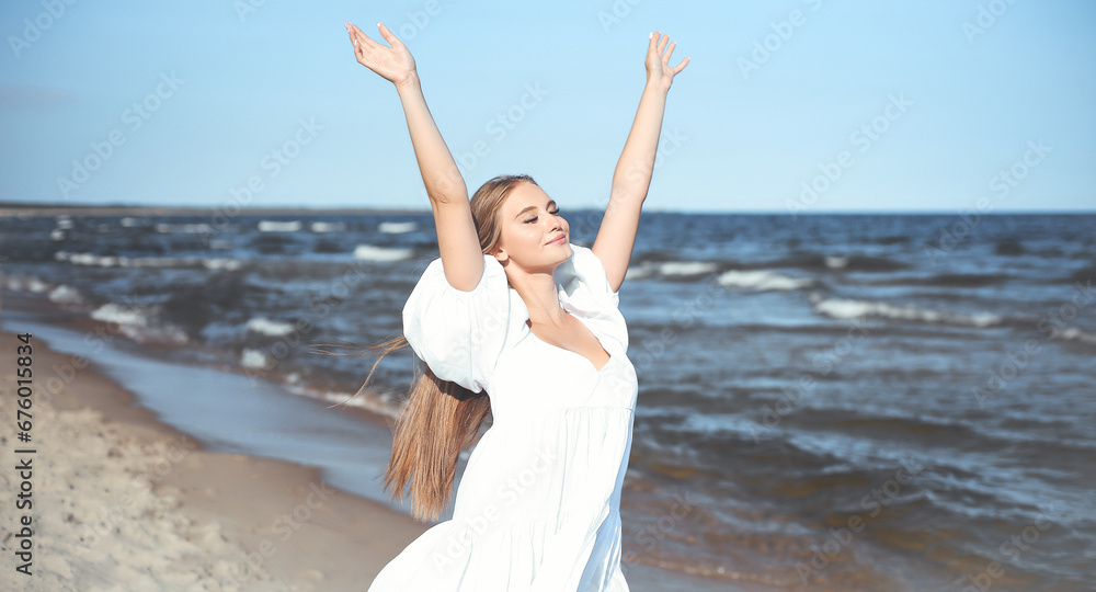 Happy smiling beautiful woman on the ocean beach standing in a white summer dress, raising hands Happy smiling beautiful woman on the ocean beach standing in a white summer dress, raising hands