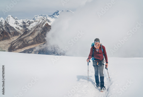 Smiling climber in sunglasses with backpack and trekking poles ascending Mera peak high slopes at 6000m enjoying legendary Mount Everest, Nuptse, Lhotse with South Face wall beautiful High Himalayas. photo