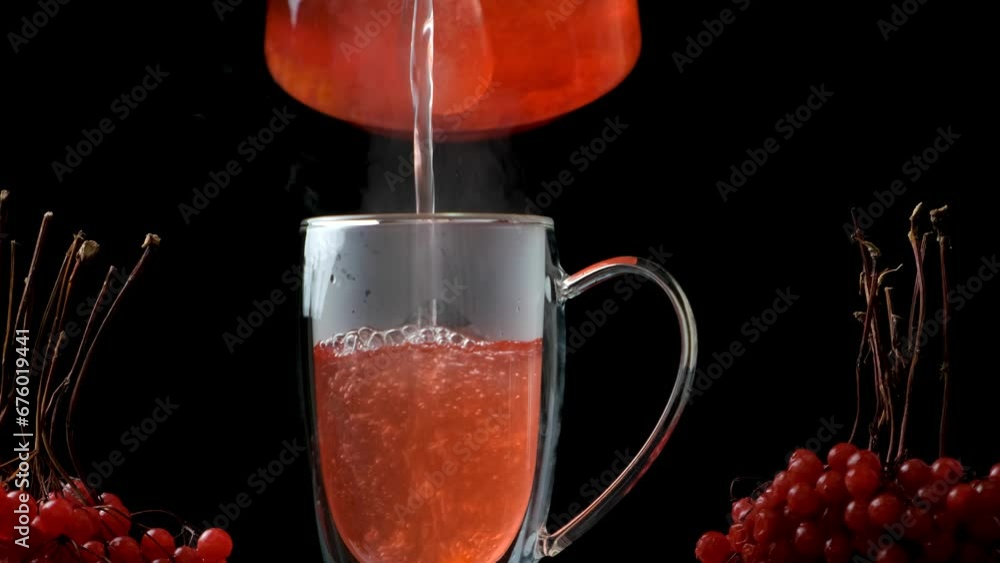Hot viburnum tea pouring into a cup from a teapot on a black background ...