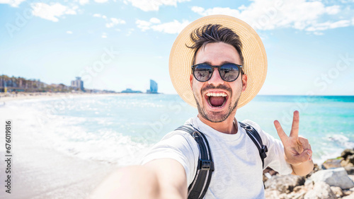 Happy man with hat and sunglasses taking selfie picture with smartphone at the beach - Cheerful traveler having fun outside - Handsome guy smiling at camera