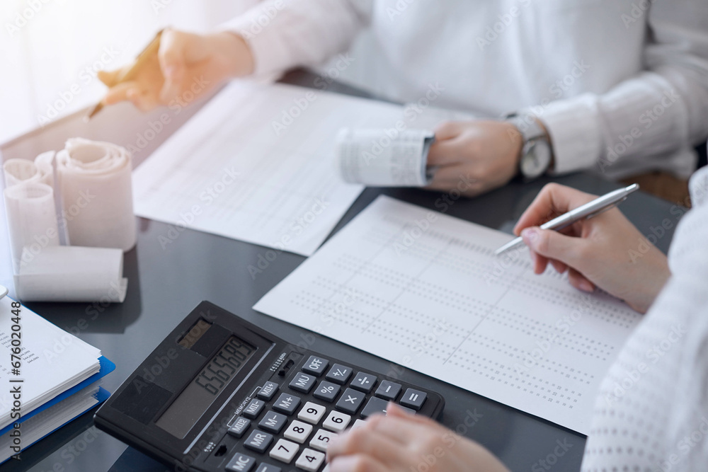 Two accountants use a calculator and laptop computer for counting taxes or revenue balance. Business, audit, and taxes concepts Two accountants use a calculator and laptop computer for counting taxes or revenue balance. Business, audit, and taxes concepts