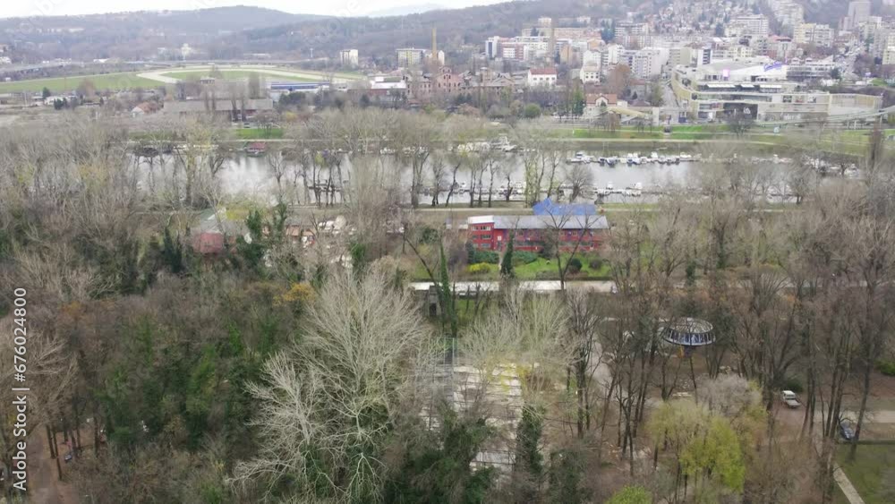 Drone shot starting from a peaceful suburban lake and ascending to reveal a big city