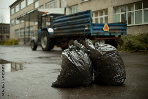 Two bags of garbage on background of tractor. Garbage collection on site. Garbage bags on road.