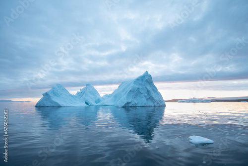 Arctic nature landscape with icebergs in Antarctica with midnight sun sunset sunrise in the horizon. Summer Midnight Sun and icebergs. Big blue ice in icefjord. Climate change global warming. 