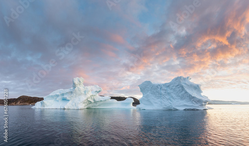 Arctic nature landscape with icebergs in Greenland icefjord with midnight sun. Early morning summer alpenglow during midnight season. Hidden Danger and Global Warming Concept. Tip of the iceberg.