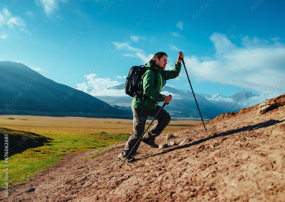Man hiker with trekking poles and backpack climbing up the mountain