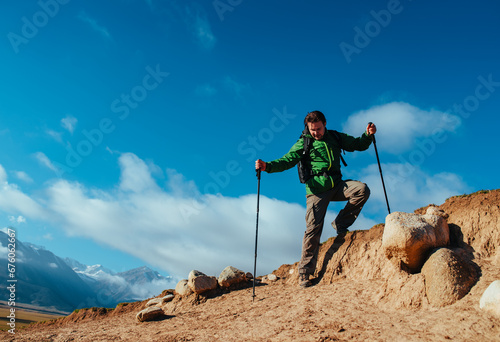Man hiker with trekking poles climbing down from rocks