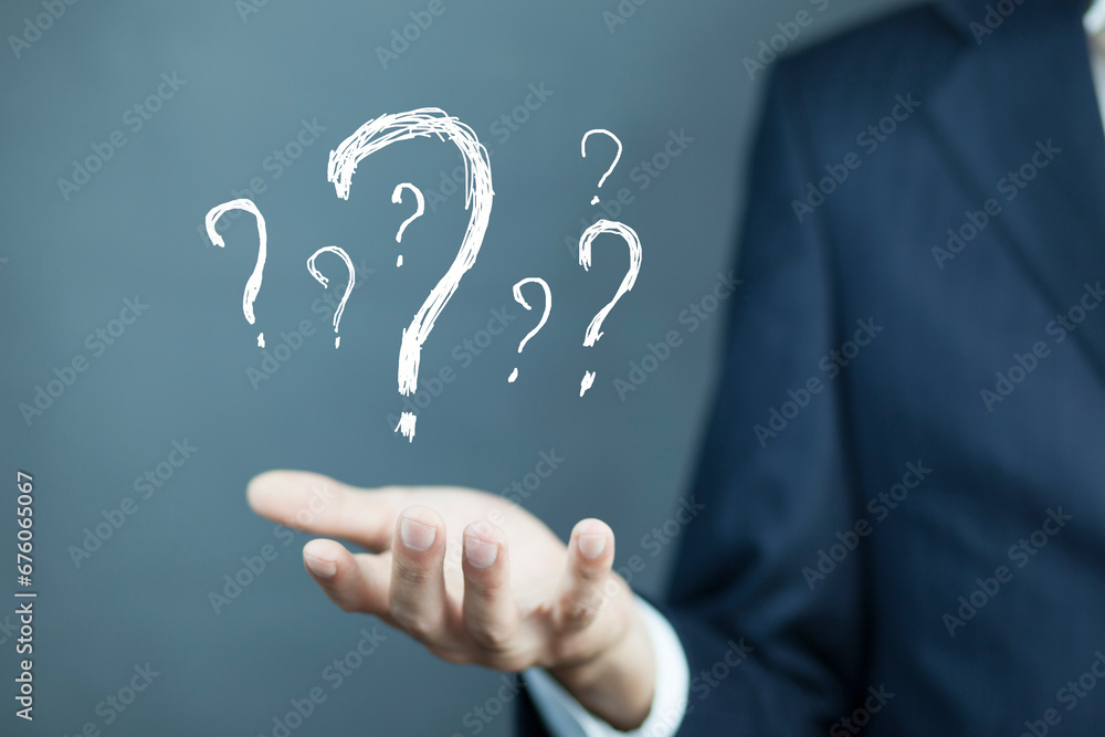 Businessman on blurred background holding hand drawn question marks Businessman on blurred background holding hand drawn question marks