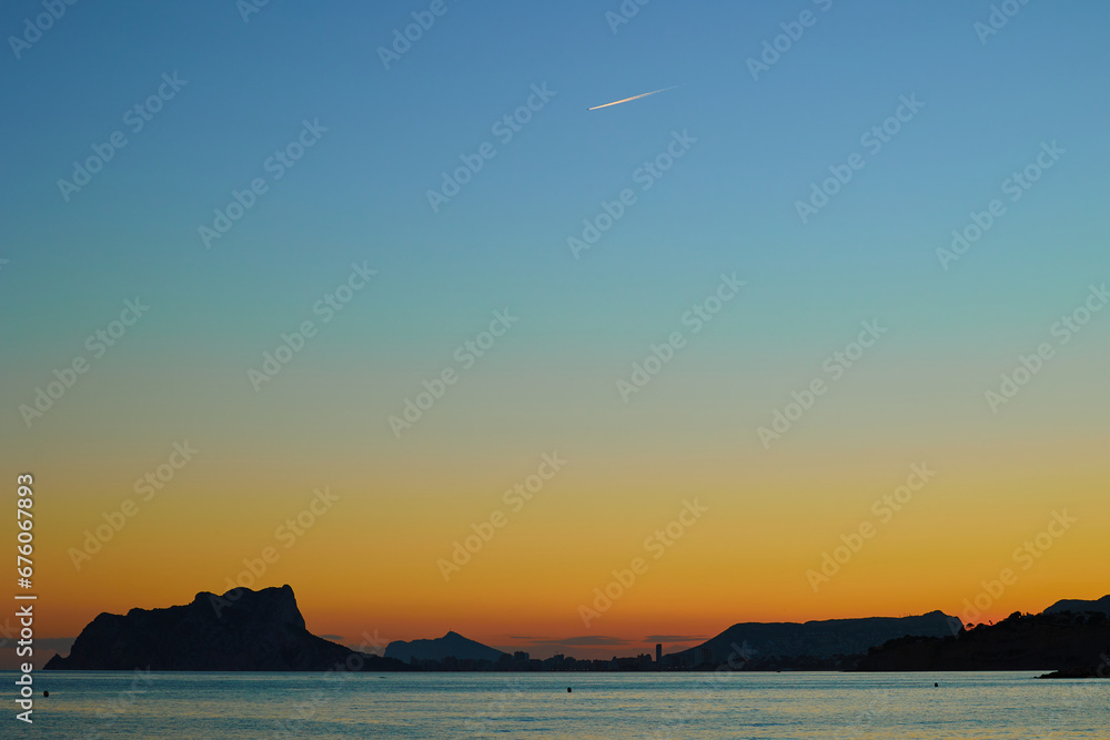 Orange and blue gradient of sunset sky over the sea and rocks in a calm Mediterranean bay