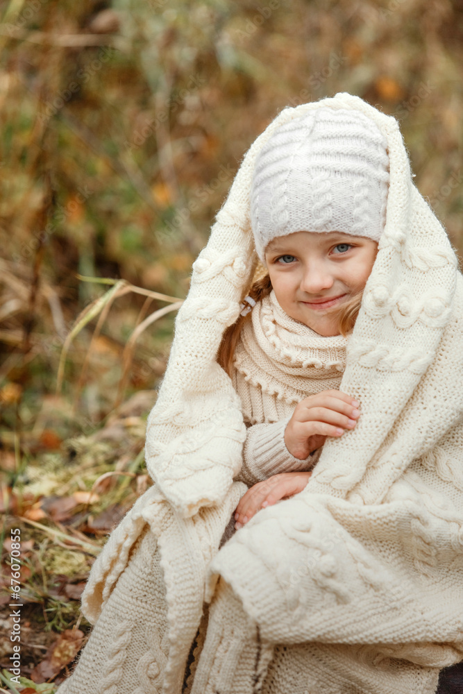 Portrait of a smiling young girl sitting in a park wrapped in a white blanket. Portrait of a smiling young girl sitting in a park wrapped in a white blanket.