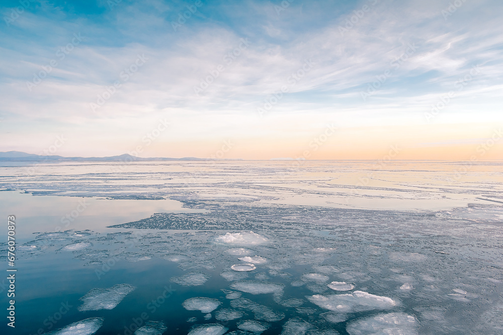Fototapeta premium Sea winter landscape. Sea slush and ice floes on the sea surface in winter during sunset. Fabulous winter day by the sea.