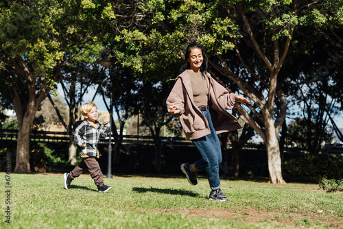 Mother and her three-year-old son run on the grass in the park, playing, hugging, smiling, and giving each other kisses