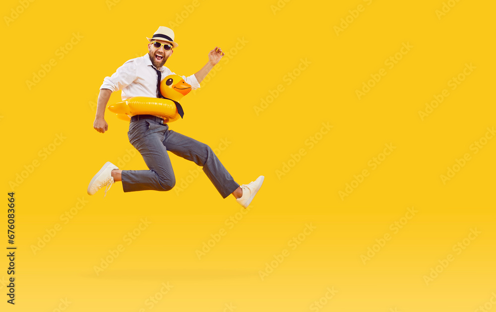 Funny happy man in office clothes, sunglasses and with duck rubber ring is going on summer holiday trip and having fun jumping on a yellow background with copy space. Vacation and travel concept.