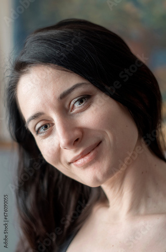 Lifestyle portrait of mid adult woman looking at camera at home. Nice female face smiling. Green Eyes. Brown-haired middle aged lady. Age from 30 to 40 years