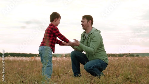 Cheerful son gives high-five to father in field with landscape view of nature beauty