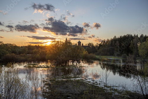 Rural landscape with a river at sunset. Evening in early spring in May. The sun is above the horizon, shining through the clouds.