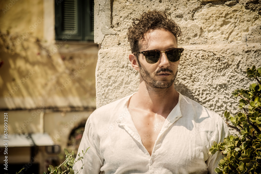 A man wearing sunglasses standing in front of a stone wall A man wearing sunglasses standing in front of a stone wall