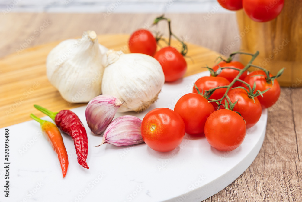 ingredients in the kitchen, vine cherry tomatoes with garlic and chilly pepper on a wooden and stone board and mortar for chopping ingredients in the kitchen, vine cherry tomatoes with garlic and chilly pepper on a wooden and stone board and mortar for chopping