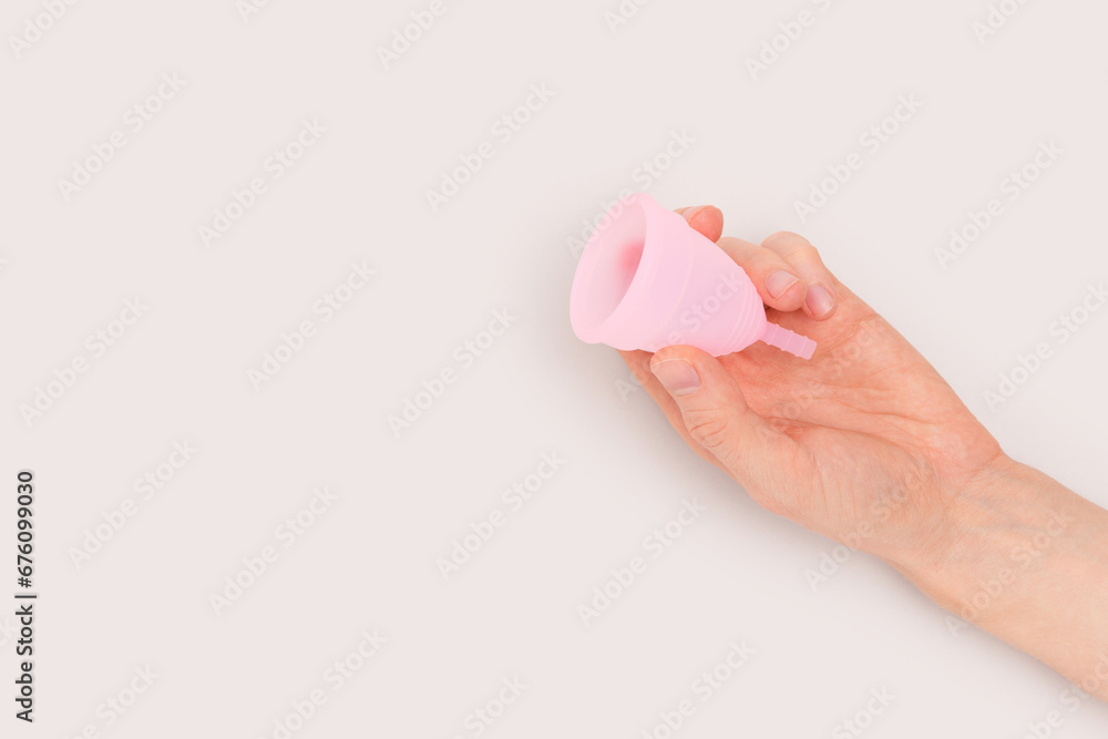 Female hand hold pink menstrual cup on a gray background. Minimal composition with copyspace. - obrazy, fototapety, plakaty 