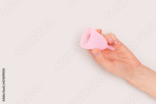 Female hand hold pink menstrual cup on a gray background. Minimal composition with copyspace. photo